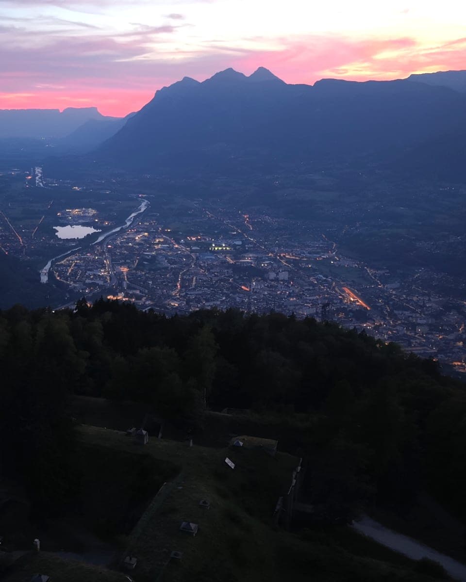 Vue aérienne au drone d’une ville de vallée au crépuscule, les lumières s’allument sous un ciel rose